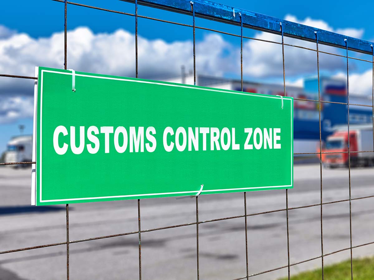 Customs clearance sign on the territory of the logistics customs terminal, with temporary storage of goods at the bonded warehouse. Trucks stand near the unloading and loading area.